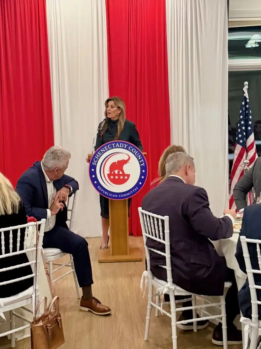 The committee chairwoman speaking at a lectern bearing the committee seal at a committee dinner